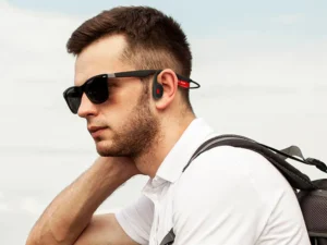 Homem usando fones de ouvido de condução óssea e óculos de sol ao ar livre.