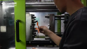 Worker sampling custom-colored open-ear headphone parts from an injection molding machine.
